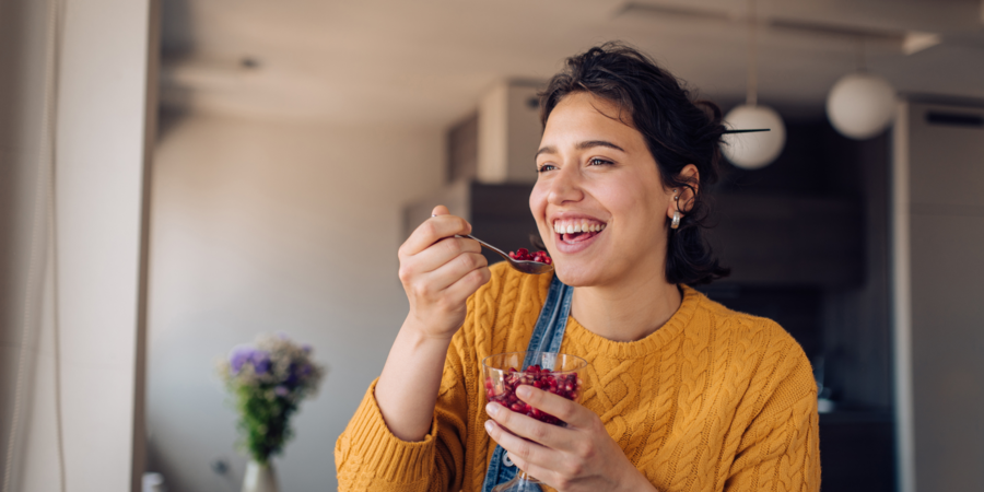 Een jonge vrouw eet fruit terwijl ze al lachend nadenkt over haar emoties.